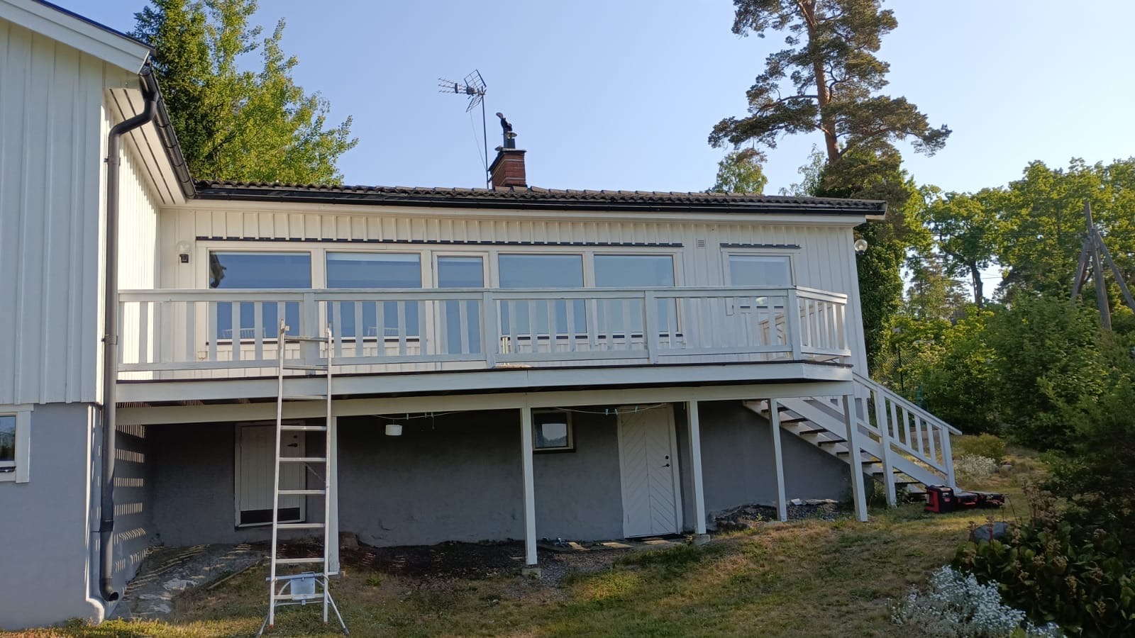 Lång upphöjd altan med vitmålat räcke längs fasaden på ett vitt hus