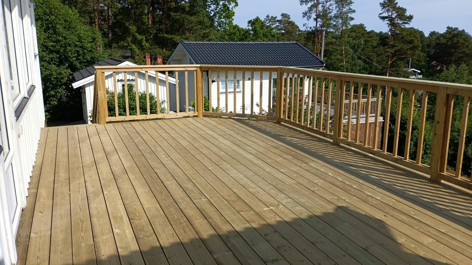 Altan i trä med rundat hörn och tätt spjälräcke mot trädgården