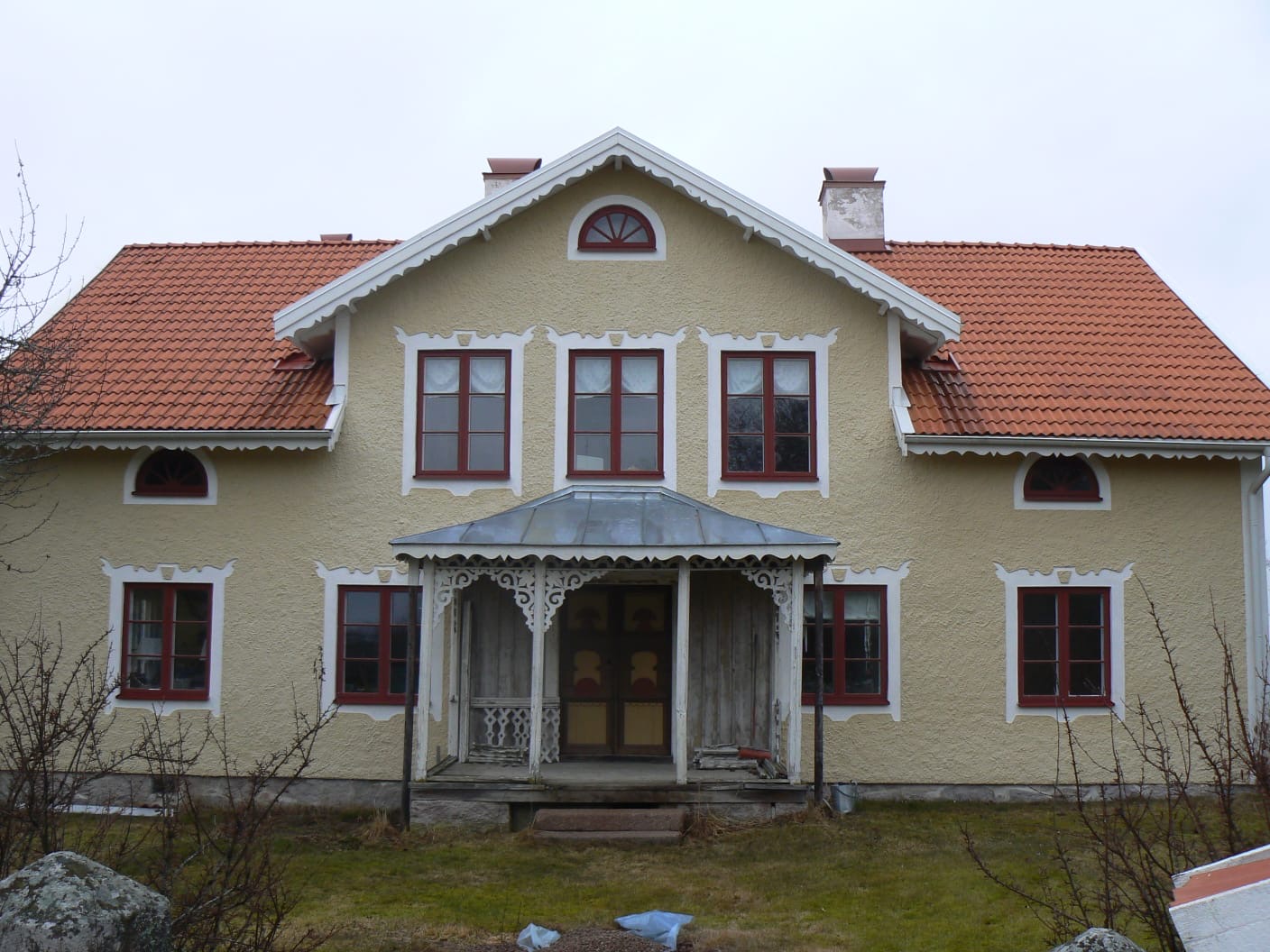 Äldre villa med lövsågad veranda under renovering